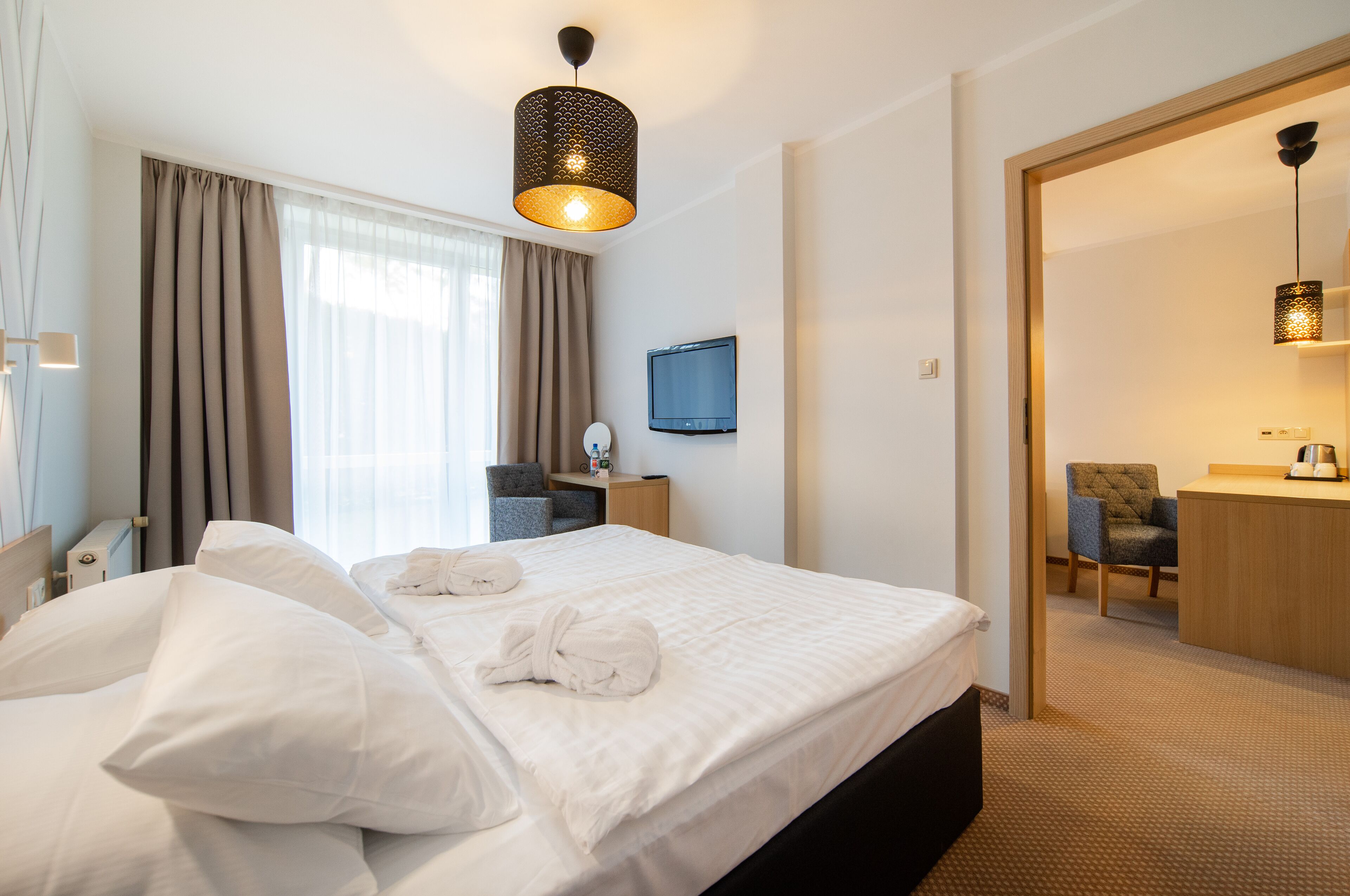 Ein Hotelzimmer mit einem großen Bett, einem Schreibtisch, einem Sessel, einem Fernseher und einem durch eine offene Tür einsehbarer Badezimmer.