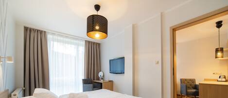A hotel room with a large bed, a desk, a chair, a television, and a bathroom visible through an open door.