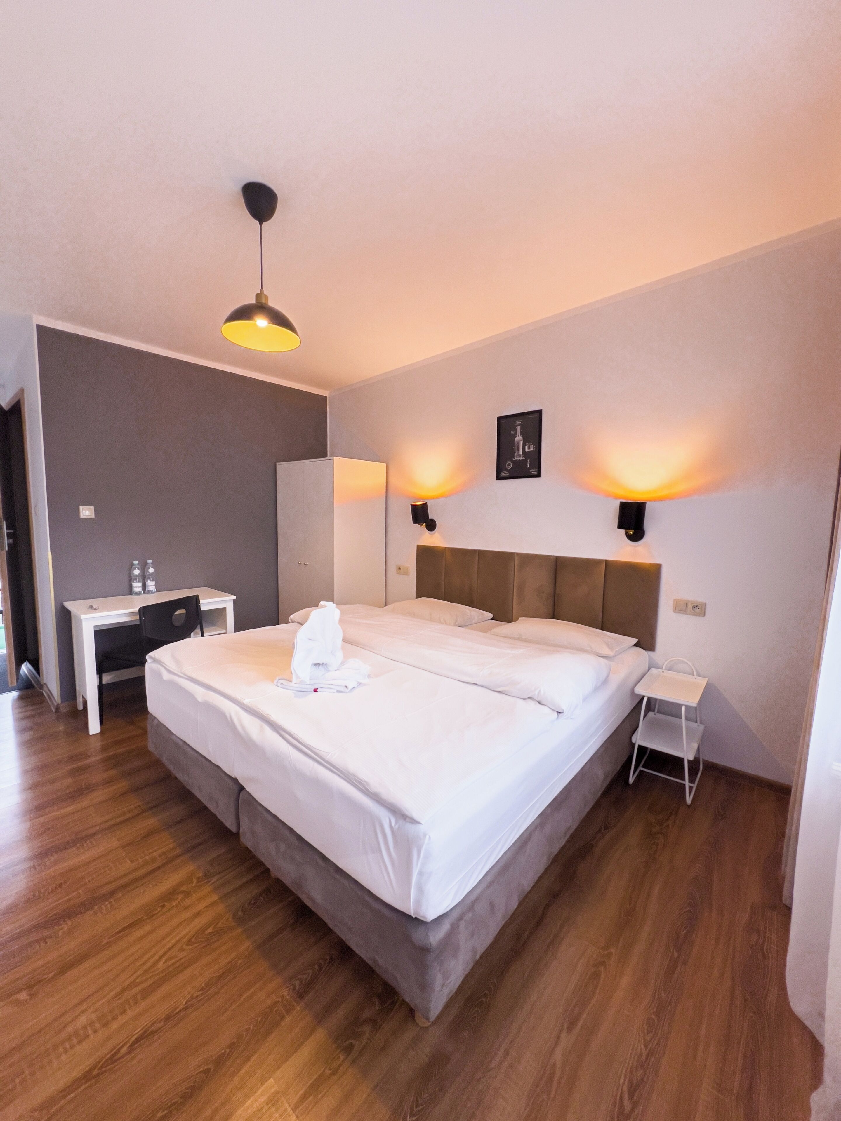 A modern hotel room with a large bed, bedside tables, a desk, and a small chair.