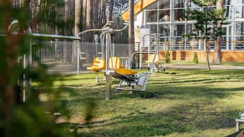 A fitness area with exercise equipment, a building with large windows, and a fenced area with trees.