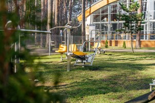 A fitness area with exercise equipment, a building with large windows, and a fenced area with trees.