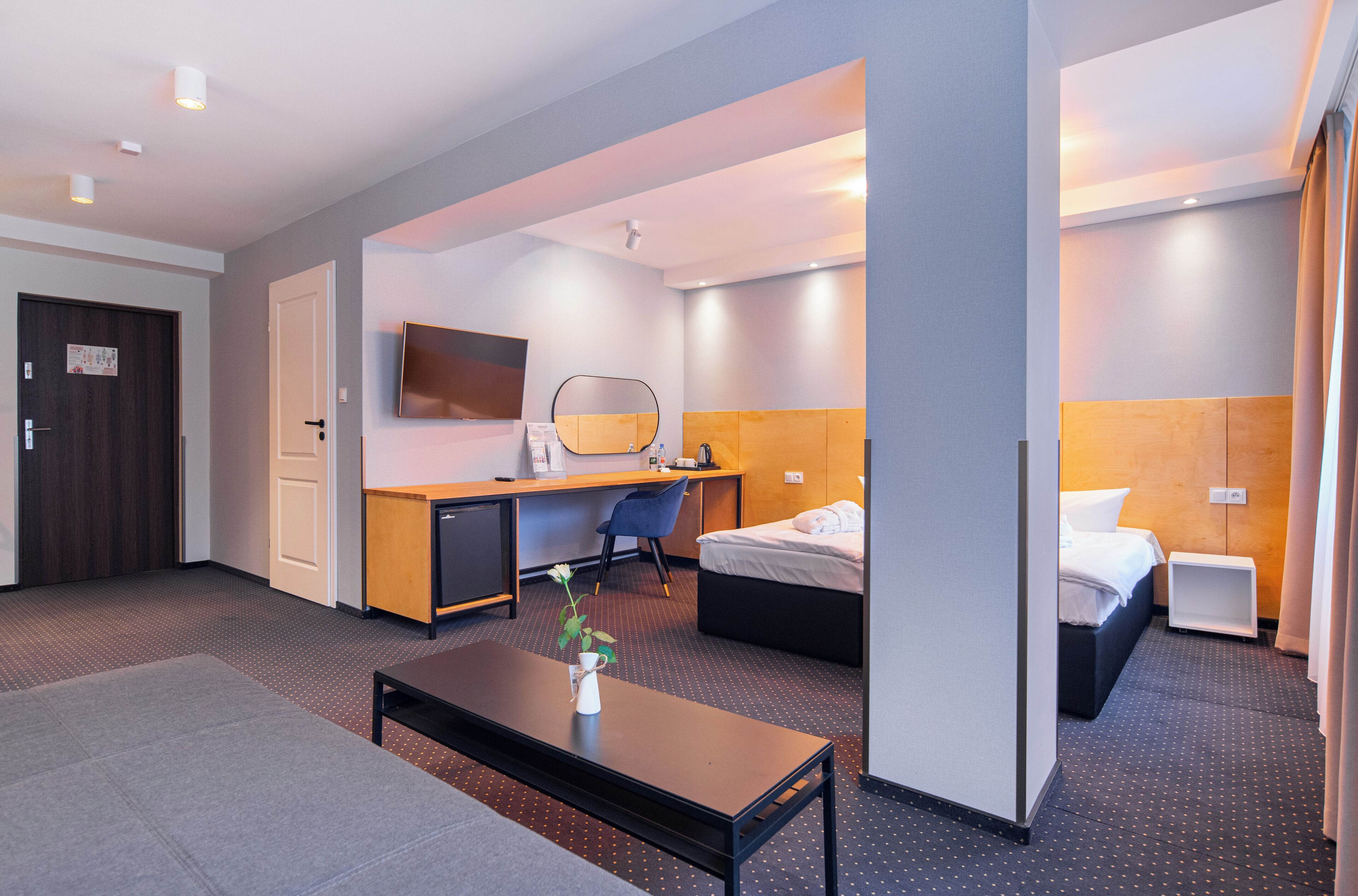 Une chambre d’hôtel avec un lit, un bureau, une chaise et une petite table sur laquelle se trouve un vase.