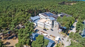 Vista aérea de um resort com um edifício grande, rodeado por uma floresta densa, e o oceano ao fundo.
