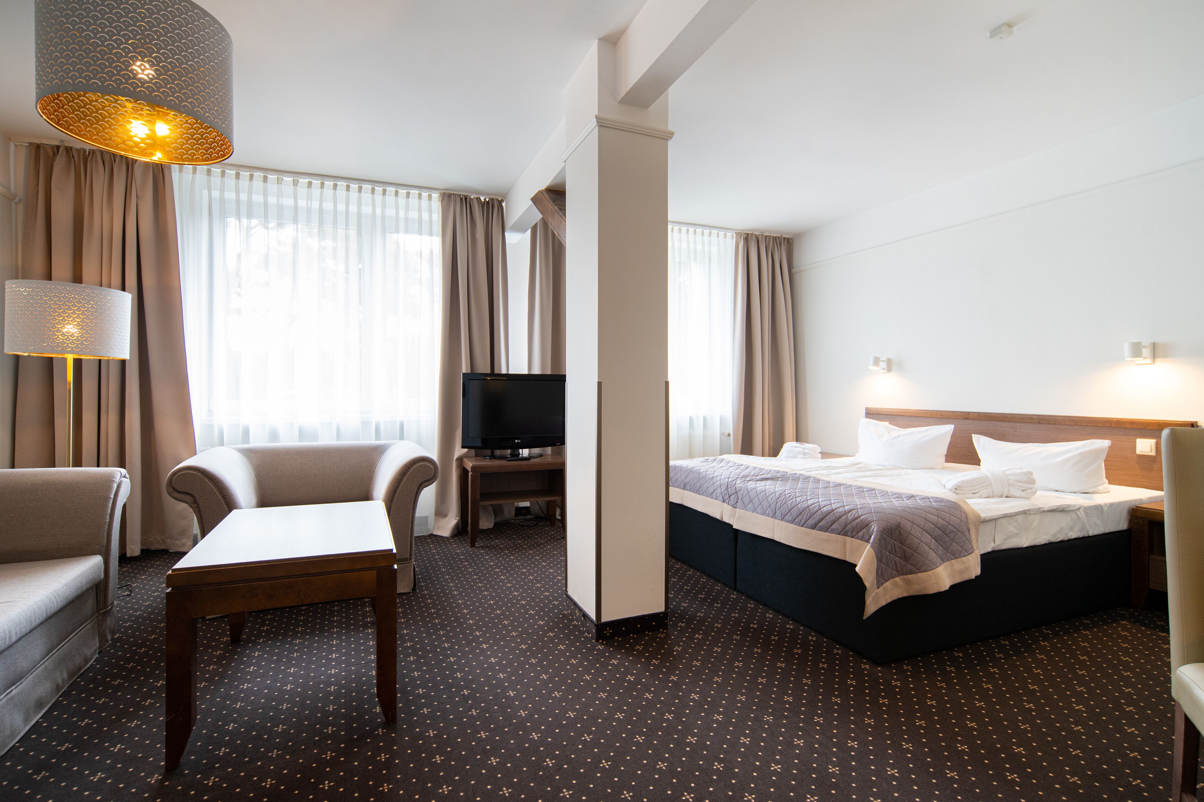 A hotel room with a bed, a desk, a chair, a television, and a lamp.