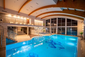 An indoor swimming pool with a wooden ceiling and glass walls, surrounded by a seating area and a staircase. - Marena Wellness & Spa (Dziwnów)