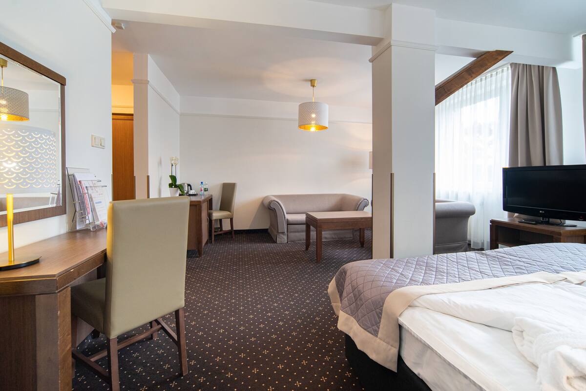 A hotel room with a bed, a desk with a chair, a television, and a window with curtains.