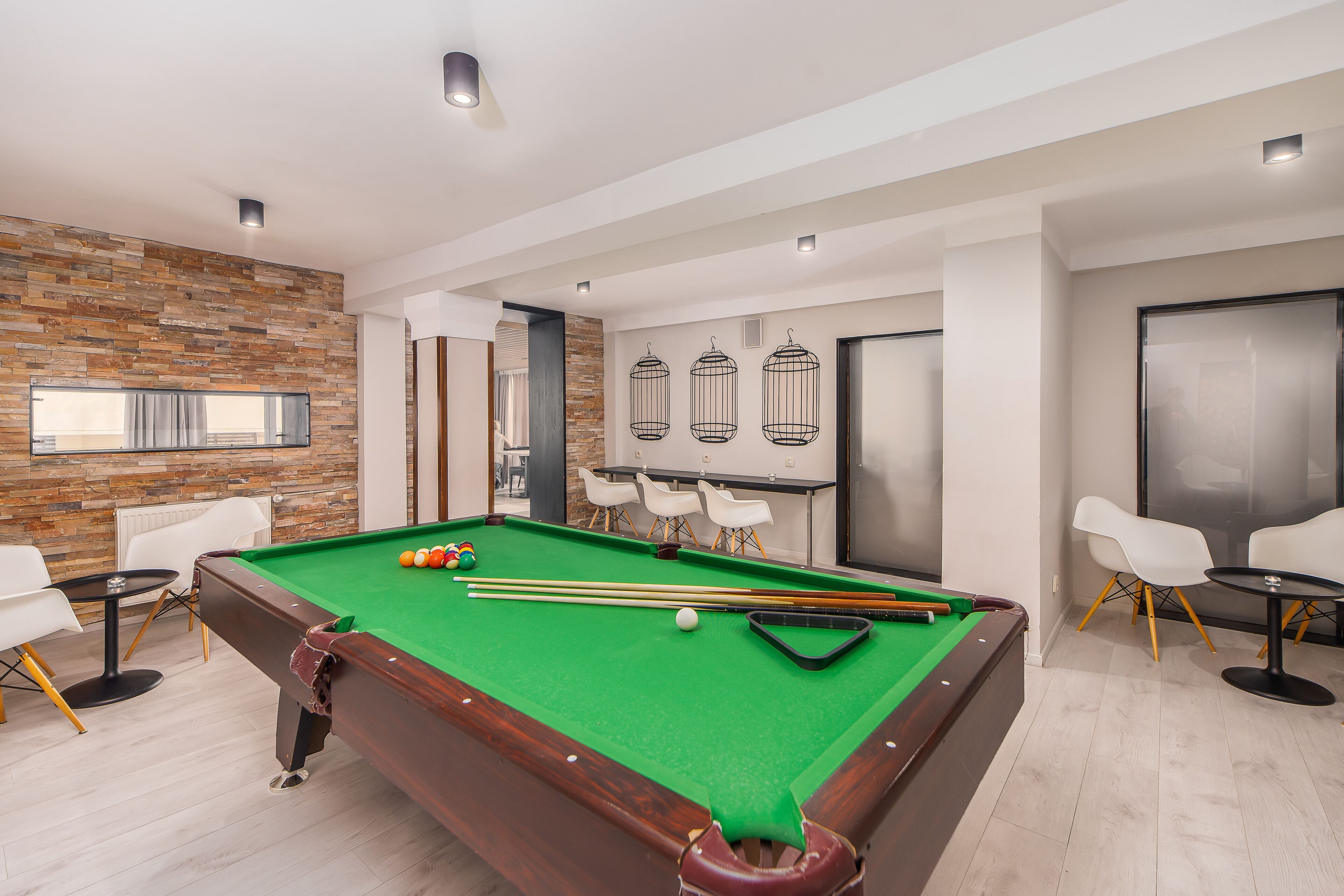 A modern pool table with a green felt surface, surrounded by white chairs and a small round table.