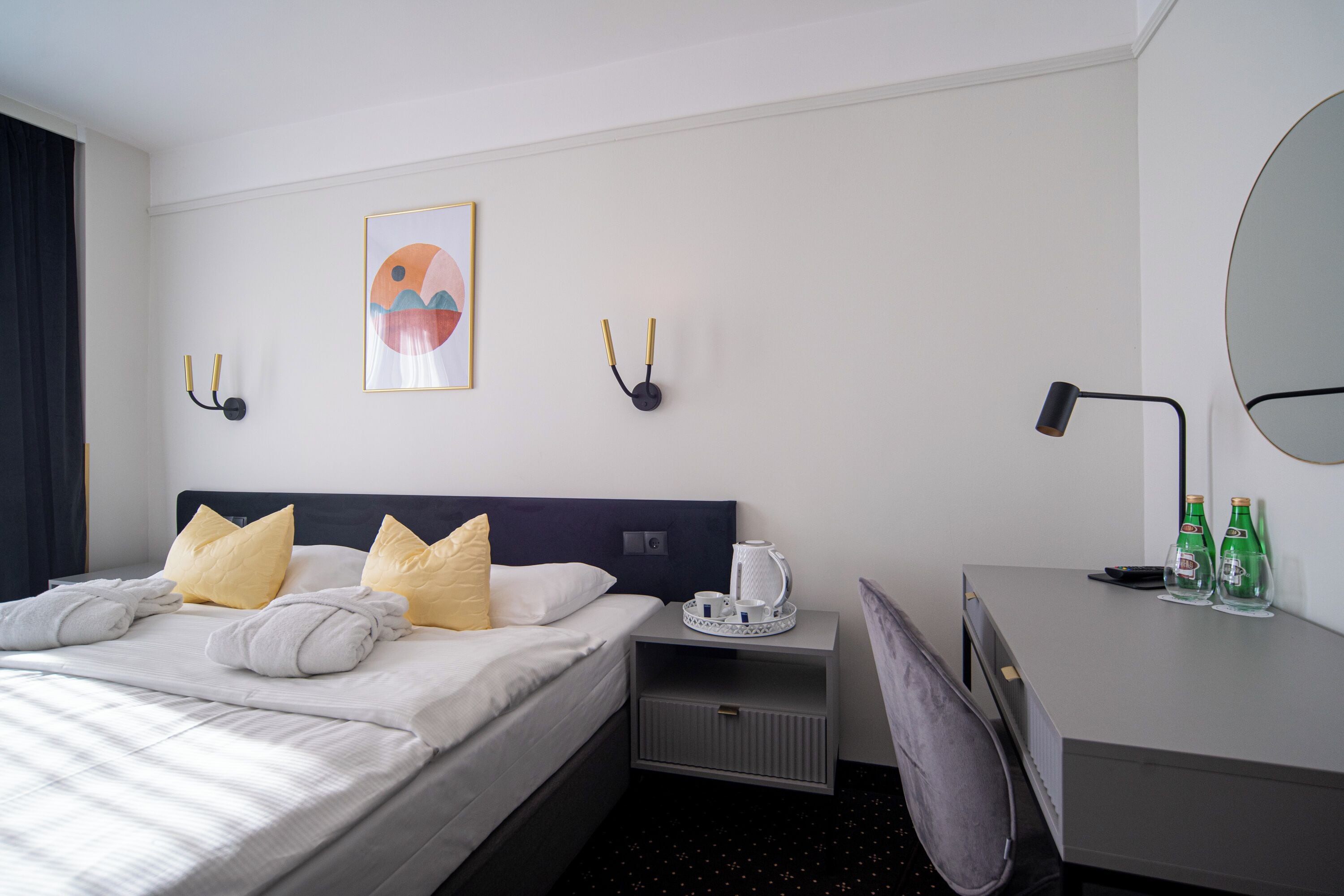 Habitación de hotel con una cama bien hecha, un escritorio con silla, una mesita de noche con lámpara y una obra de arte colgada en la pared.