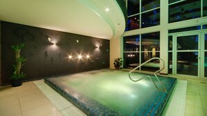 Uma área de spa com uma banheira de hidromassagem grande, uma parede curva com obras de arte e uma porta de vidro que dá para uma área de piscina.