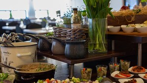 Uma mesa de jantar com diversos pratos, uma panela grande e um vaso de vidro com folhas verdes.