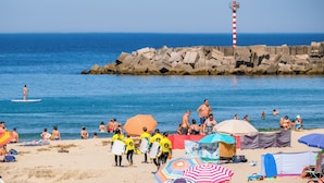 A beach with people, umbrellas, and a lighthouse.