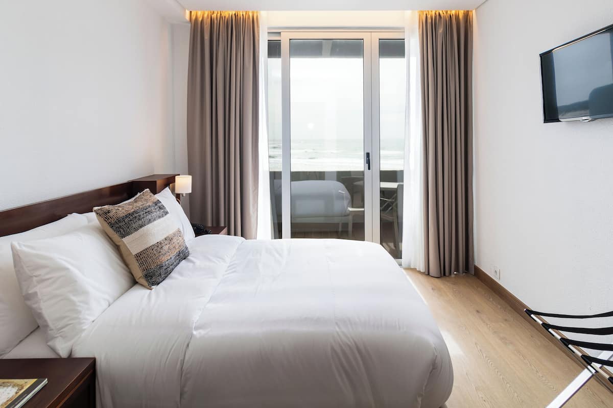 Habitació d'hotel amb un llit, una televisió penjada a la paret, una cadira i vista a l'oceà a través d'una porta corredissa.