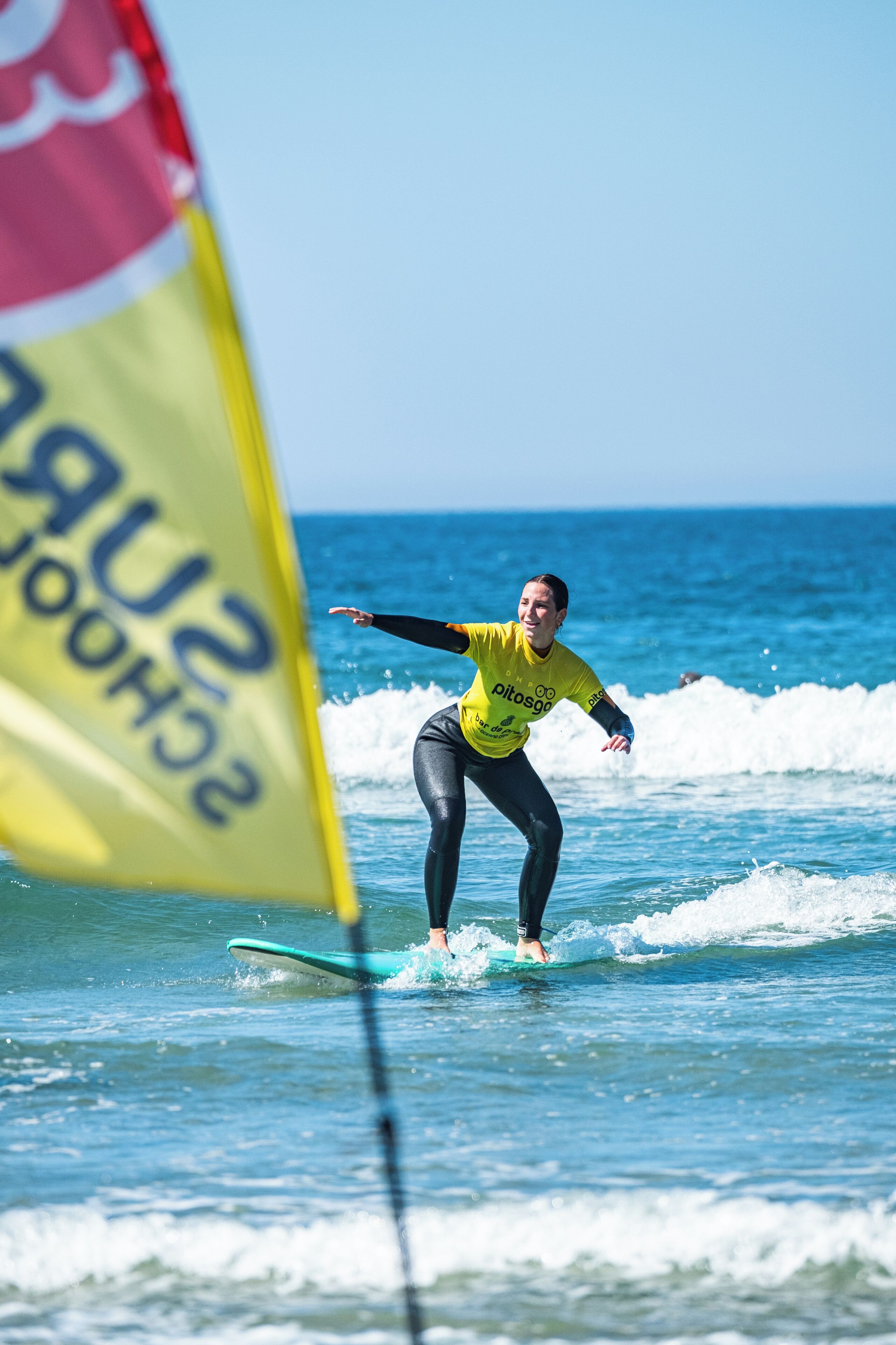 Une personne fait de la planche à voile sur une vague, avec un drapeau jaune en arrière-plan.
