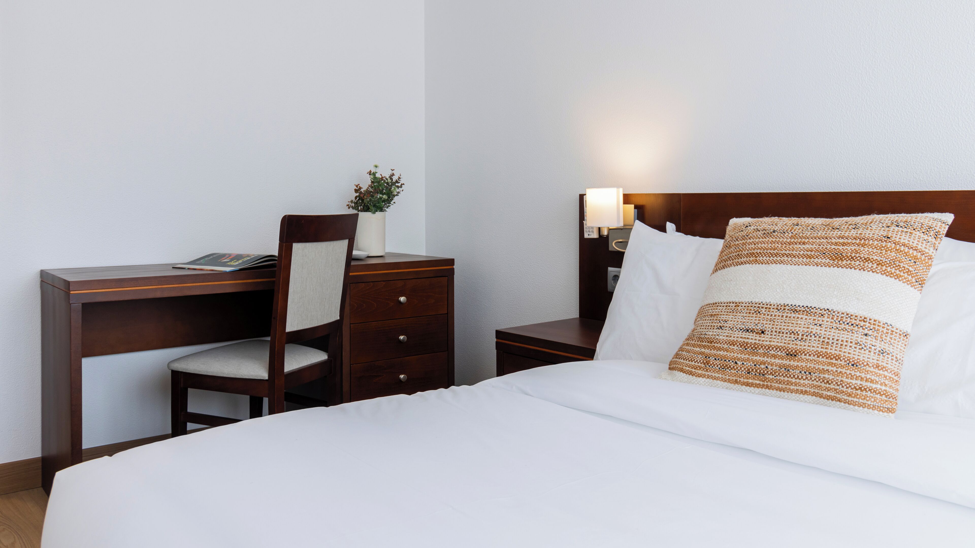 Una habitación de hotel con cama, escritorio, silla, mesita de noche y lámpara.