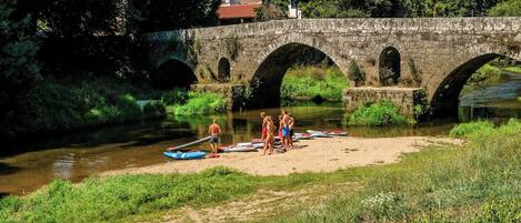 Eine Steinbrücke über einem Fluss, mit Personen und Booten am Ufer.
