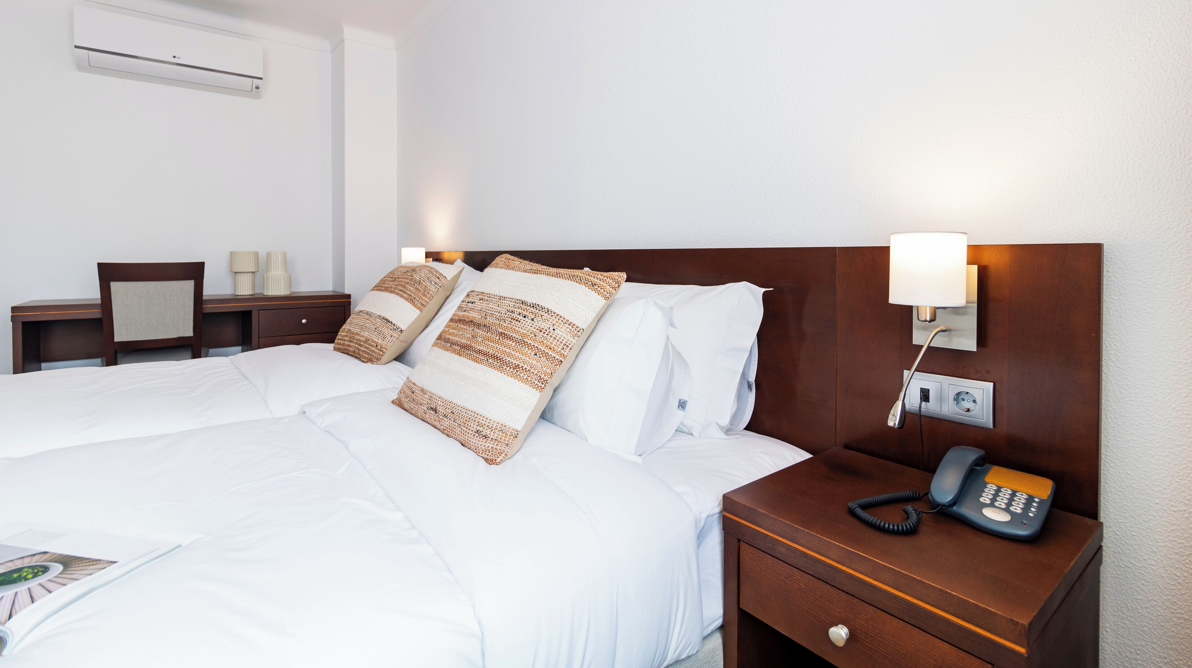 Habitación de hotel con una cama grande, una mesita de noche de madera con un teléfono y una lámpara de pared.