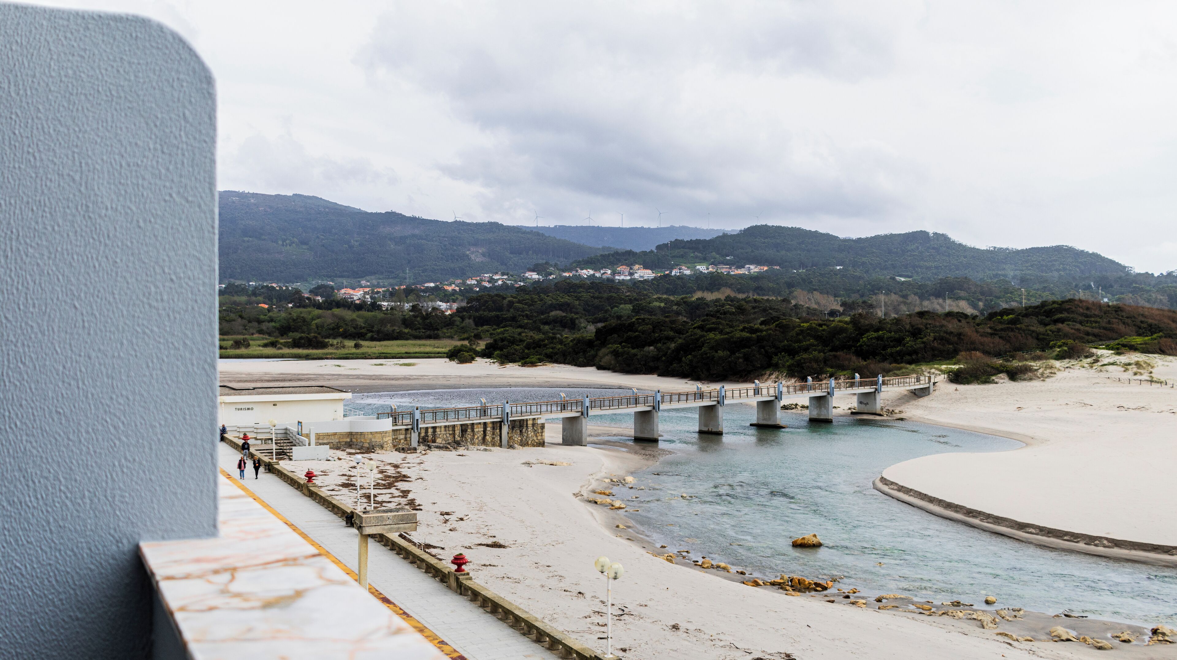 Zona costera con un puente sobre un río, una playa y montañas al fondo.