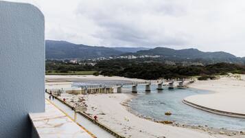 Zona costera con un puente sobre un río, una playa y montañas al fondo.