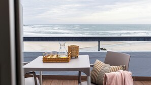 Un balcon avec une table dressée pour deux, donnant sur une plage où l’on peut admirer les vagues.