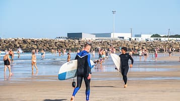 A beach with people walking and carrying surfboards.