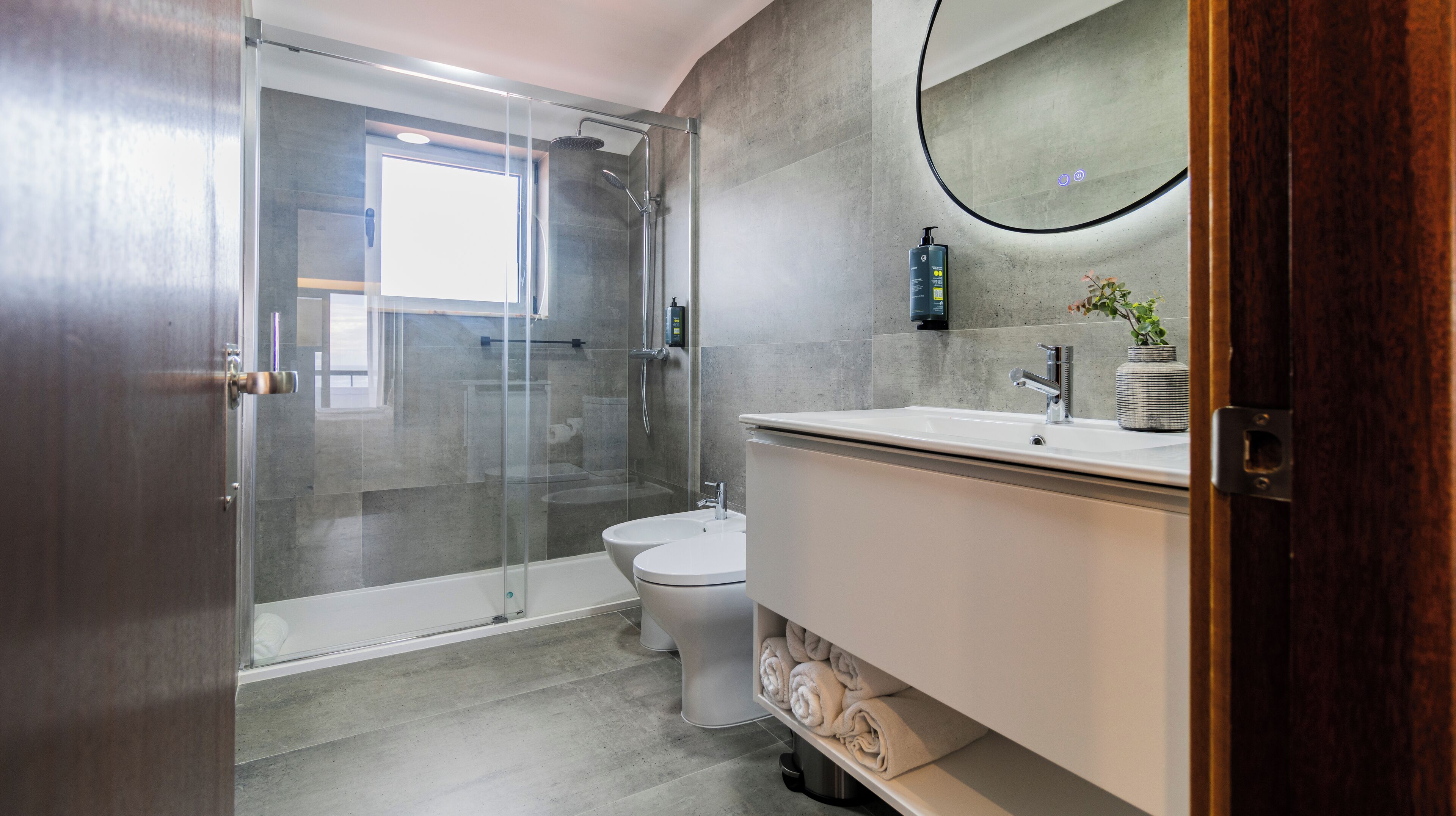 A modern bathroom with a glass-enclosed shower, a toilet, and a sink with a mirror.