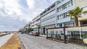 A coastal street with a row of buildings, including a hotel named 'Albergaria' with a visible 'P' parking sign.