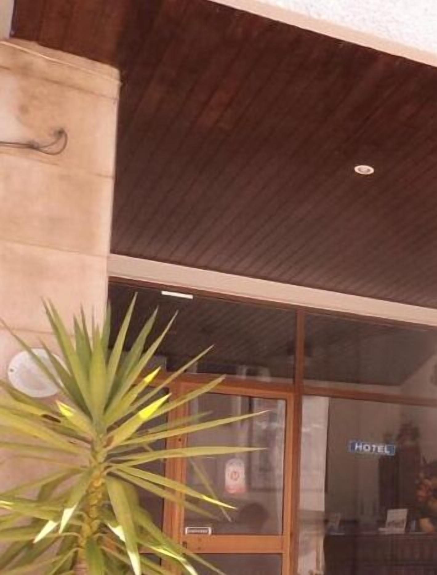 Entrada de un hotel con techo de madera, puerta de cristal y un cartel que dice 'HOTEL'.