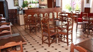 A restaurant with wooden tables and chairs, a bar area with bottles, and a view of flowers through the window. - Hotel Dona Leonor (Caldas da Rainha)