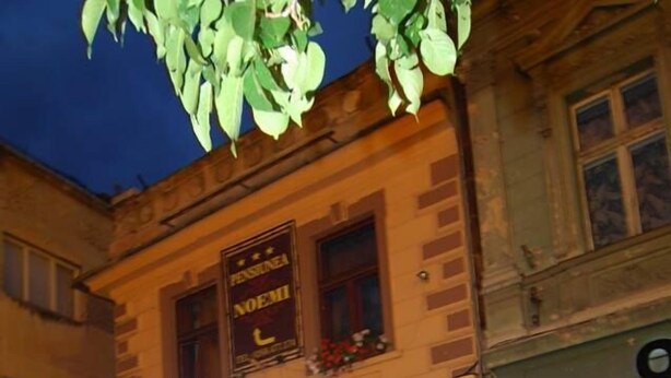 An outdoor seating area with tables and chairs in front of a building with a sign that reads "PENSIUNEA NOEMI". - Pension Noemi (Brasov)