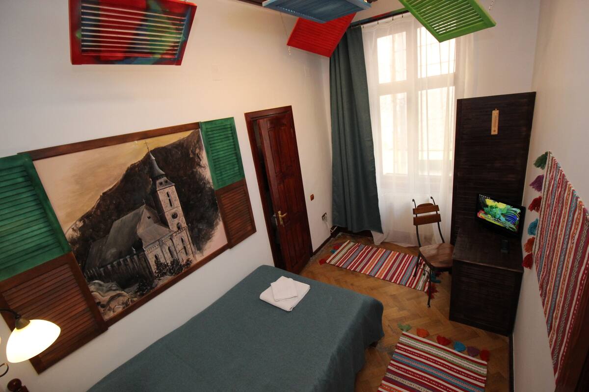 Um quarto pequeno e aconchegante com uma cama, um quadro, uma escrivaninha e uma cadeira.