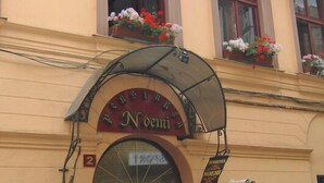 A building with a sign reading "Noemi" above the entrance, a large arched awning, and flower boxes on the windowsills. - Pension Noemi (Brasov)