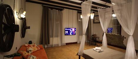 A room with a bed, a sofa, a television, and a table.