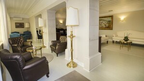 A spacious living area with leather sofas, a high ceiling, and a classic chandelier. - Hotel João Padeiro (Aveiro)