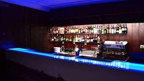 A bar area with a long counter, shelves with various bottles, and a coffee machine. - Hotel João Padeiro (Aveiro)
