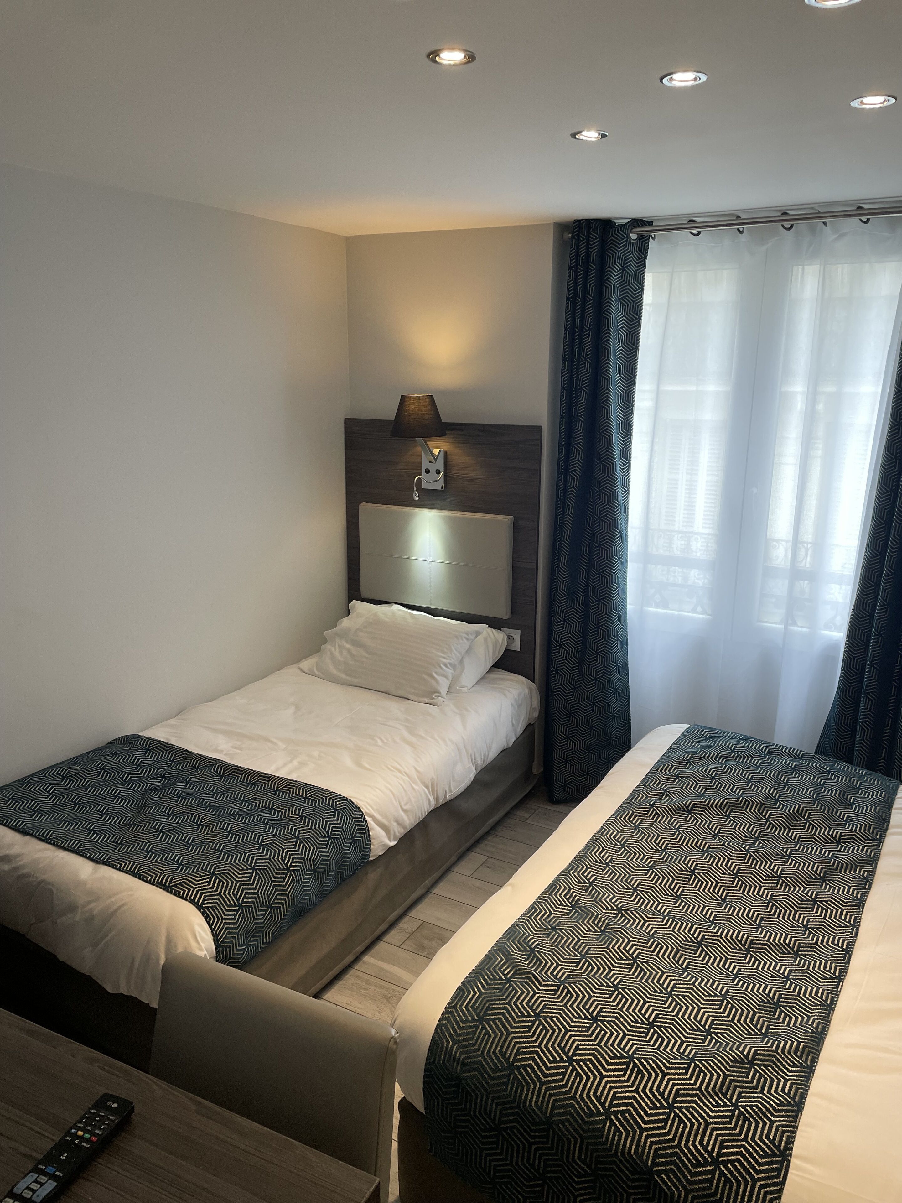 A hotel room with two beds, a nightstand, a lamp, and a remote control on the table.