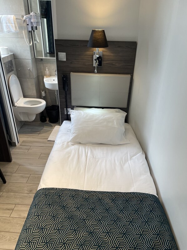 Quarto de hotel com cama, luminária de cabeceira, vaso sanitário e pia.
