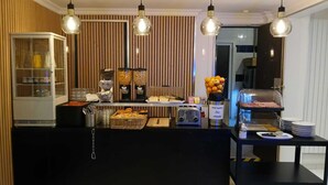 A breakfast bar with a glass display case, a coffee machine, and a fruit bowl. - Mary's Hotel République (Paris)