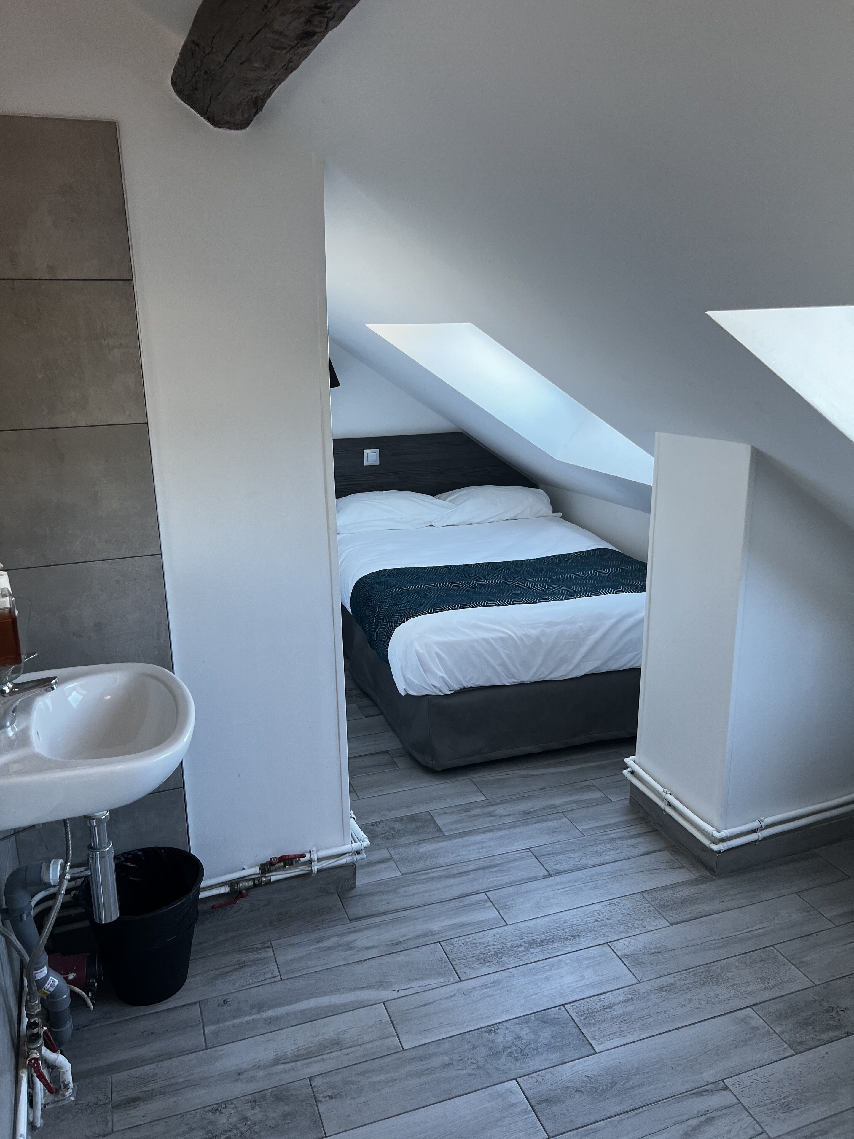 Un baño moderno con un lavamanos, un cubo negro y tuberías a la vista.