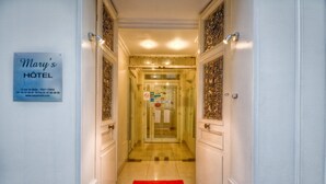 A hotel hallway with a red carpet, a sign indicating the hotel name and address, and a glass elevator door. - Mary's Hotel République (Paris)