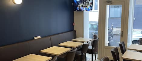 A restaurant interior with booths and tables, a television mounted on the wall, and a door leading outside.
