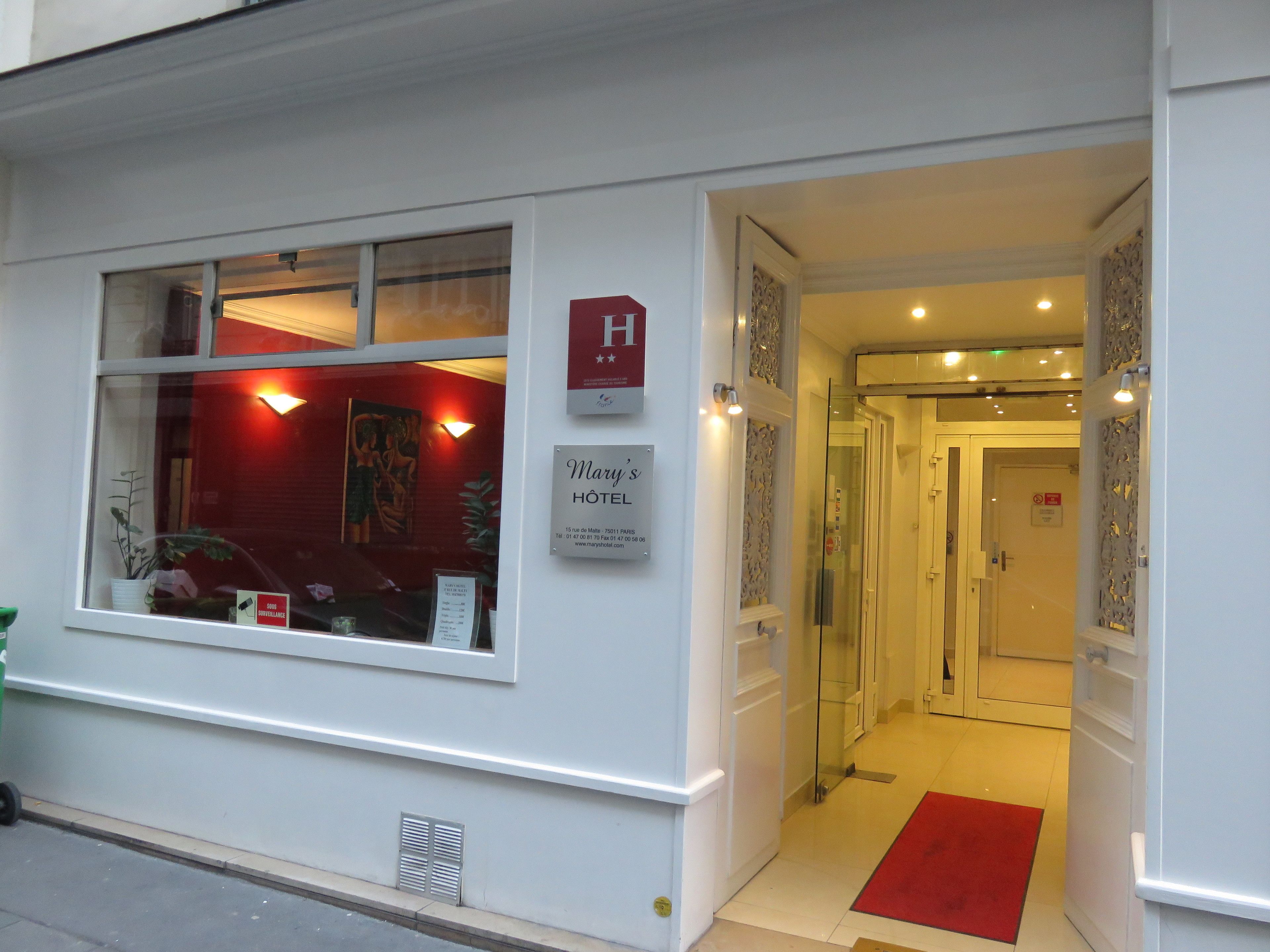 Entrada de un hotel con un cartel que dice “Mary’s HOTEL” y una señal roja con la letra “H” sobre la puerta.
