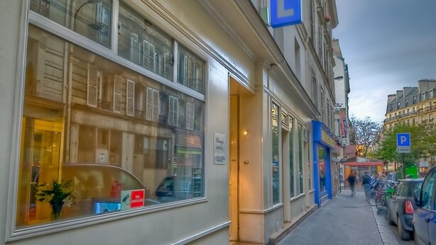 A hotel with a large blue sign, large windows, and a sidewalk with parked cars. - Mary's Hotel République (Paris)