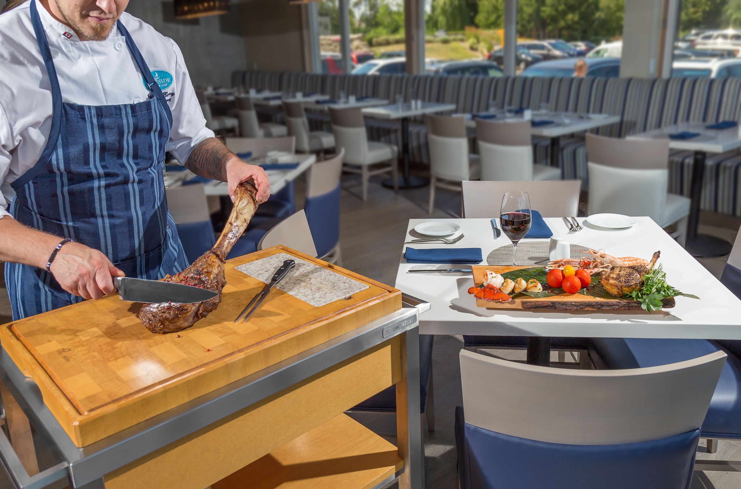 Un restaurant où un chef prépare les plats sur une planche à découper, une table dressée avec des assiettes, du vin et une variété de mets.