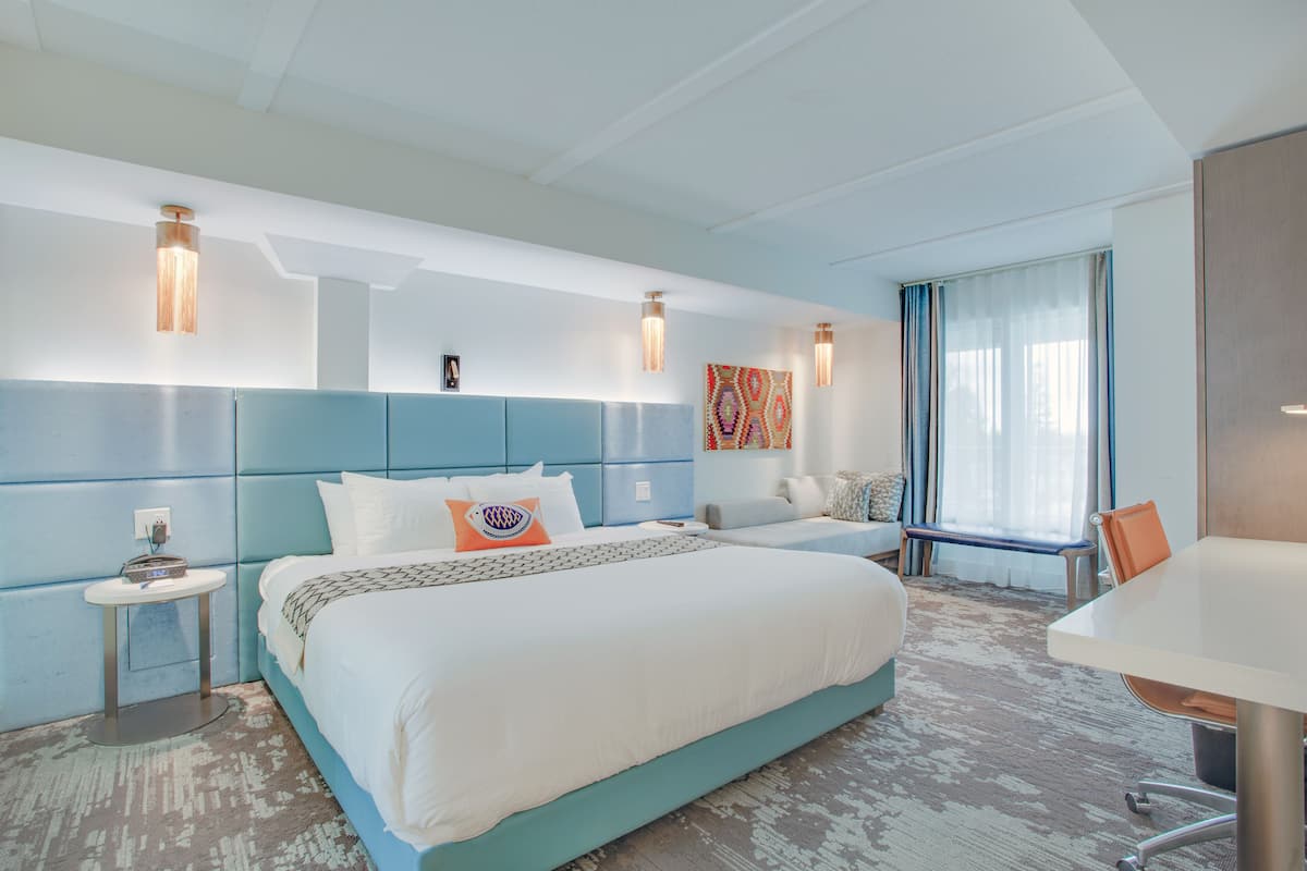 A modern hotel room with a large bed, bedside tables, a desk, and a window with curtains.