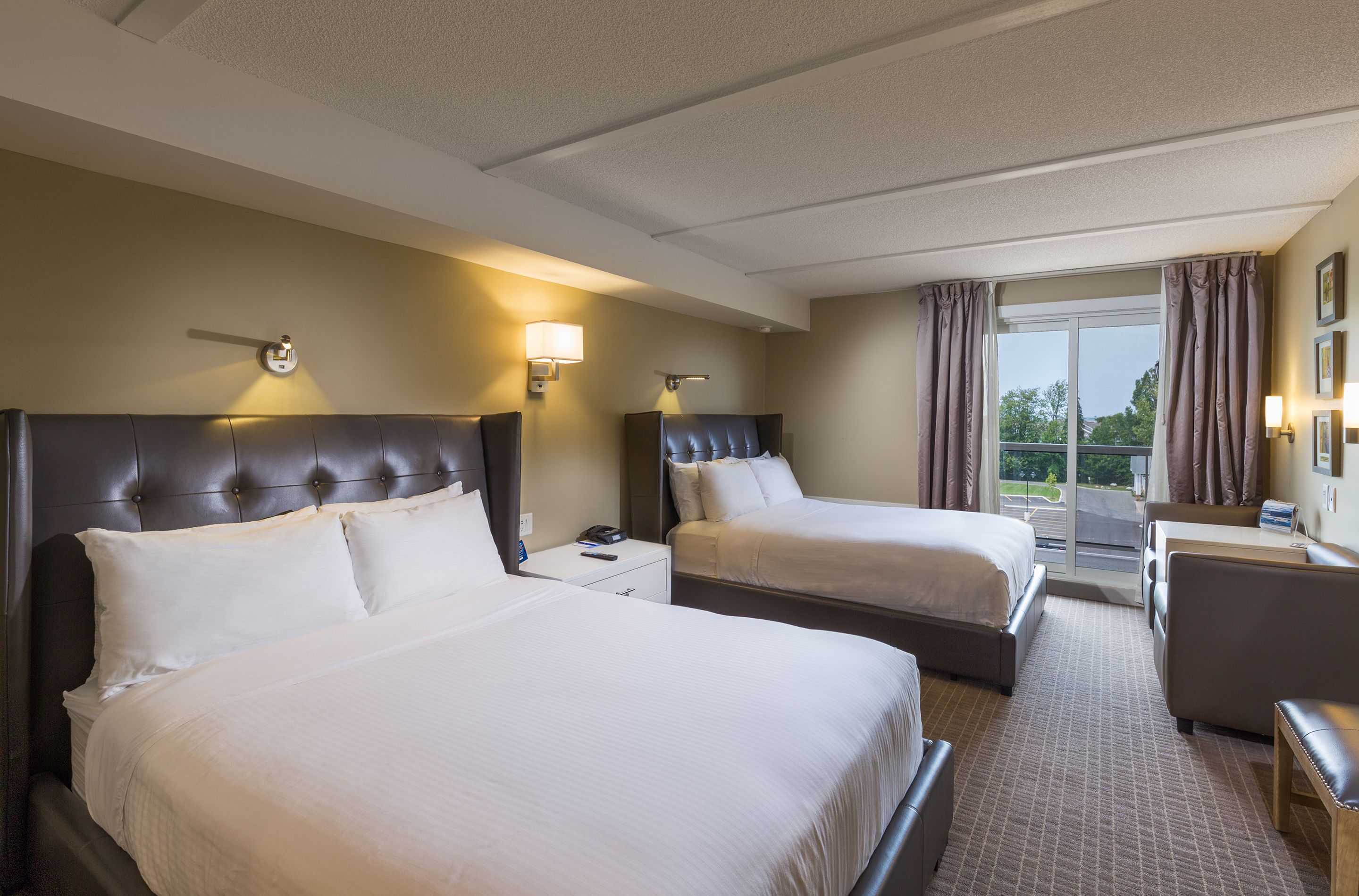 A hotel room with two beds, a desk, and a view of the outdoors.