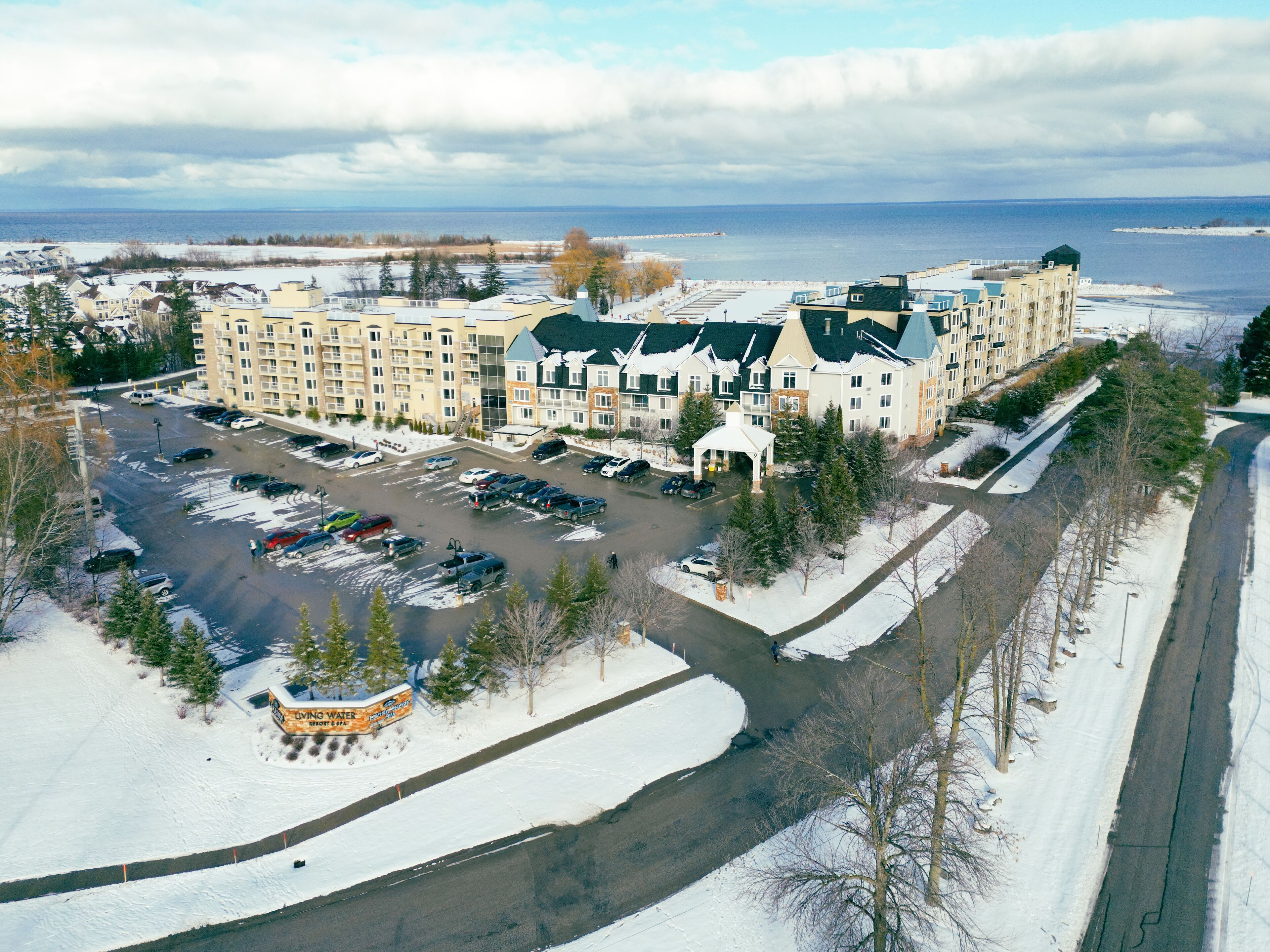 A multi-story hotel with a parking lot, a covered walkway, and a view of a body of water.
