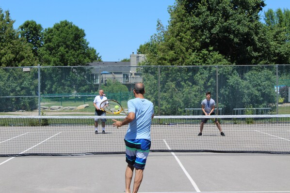 Un court de tennis avec un filet, entouré d’une clôture et d’arbres.