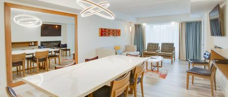 Amplia sala de estar con una gran mesa de comedor, asientos cómodos, televisor y una lámpara de araña moderna.