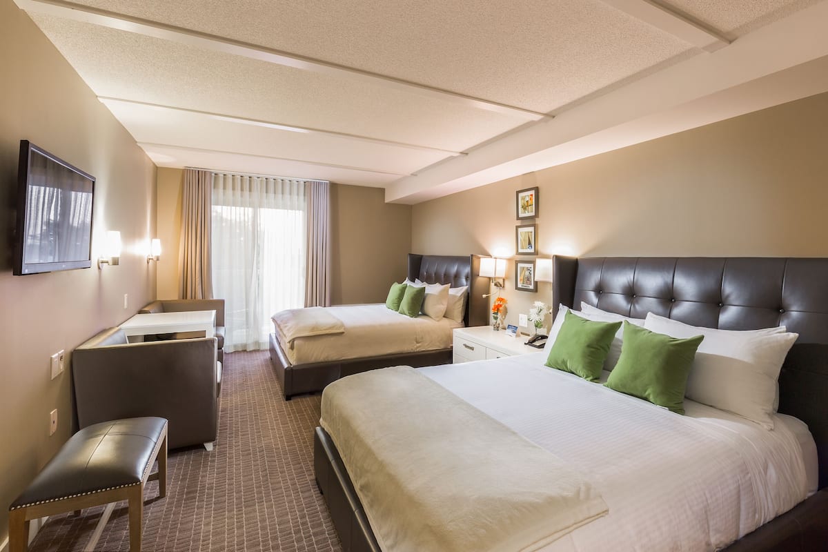 A hotel room with two beds, a desk, a chair, and a television.