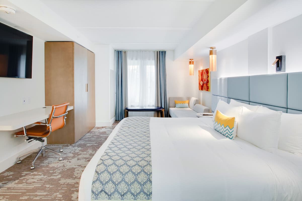 A hotel room with a large bed, a desk, a chair, a TV, and a window with curtains.